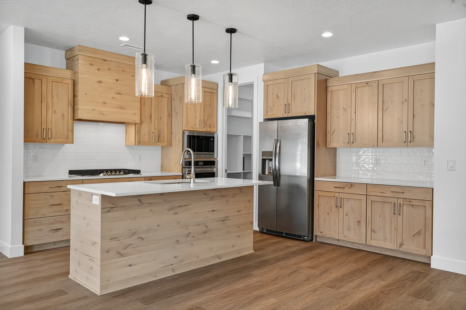 Kitchen island and wall ovens in light wood cabinetry
